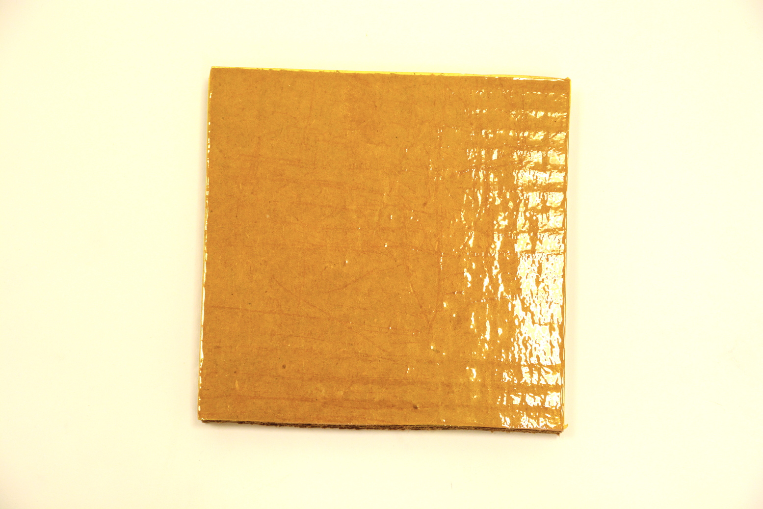 A sample cardboard square with a shiny yellow finish of Kapton tape.