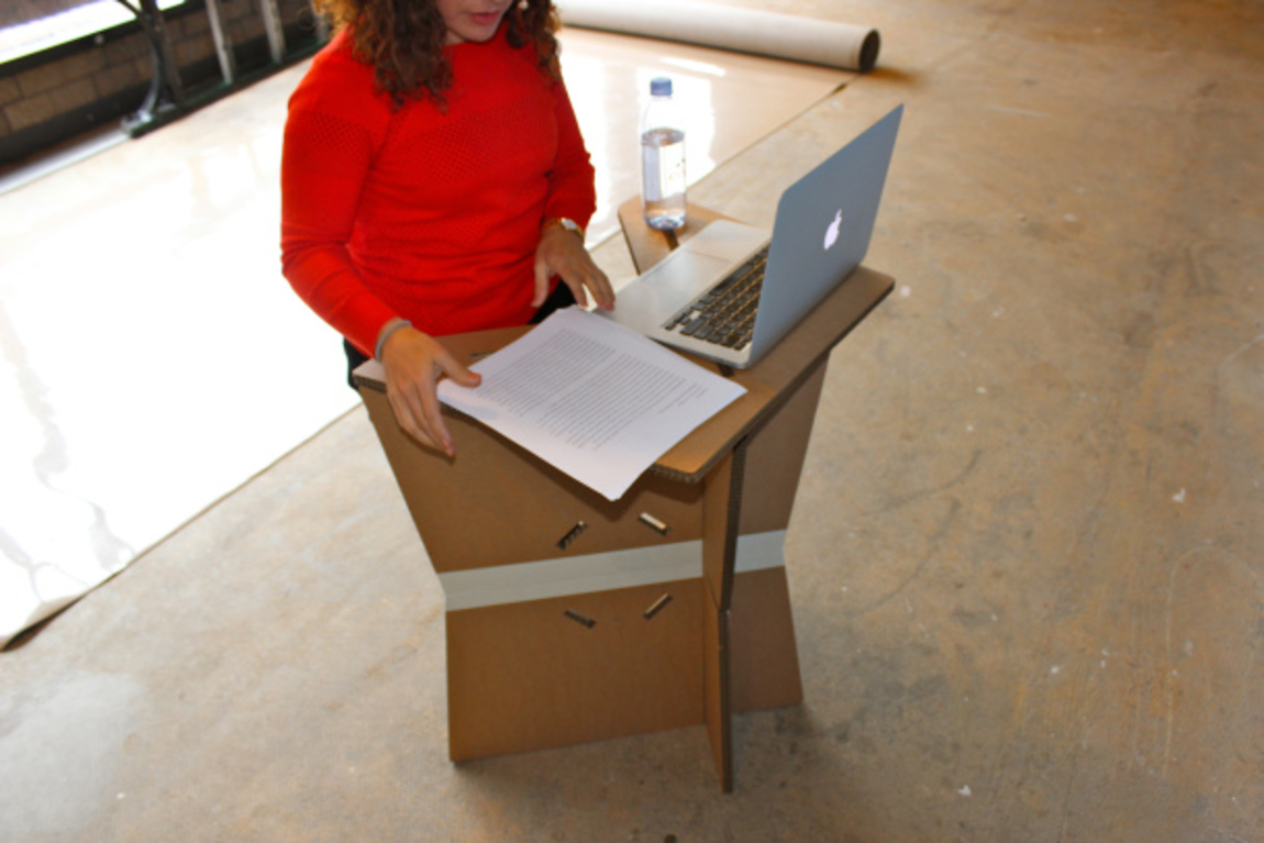 Amanda stands at the cardboard podium, testing its dimensions for her height and surface area needs.