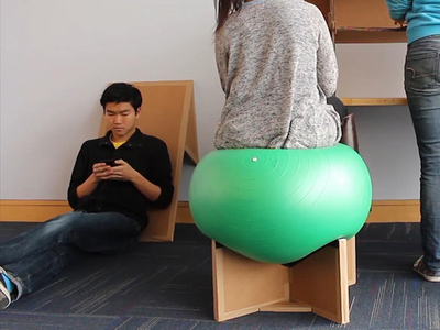 Students sit on cardboard furniture and adaptations tailored to their own bodies: standing desks, custom stools, and more.