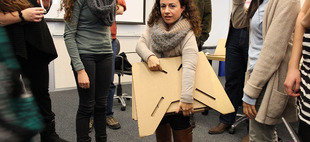Amanda Cachia, an art historian and curator who also has dwarfism, stands with a cardboard prototype of a lectern for short stature.