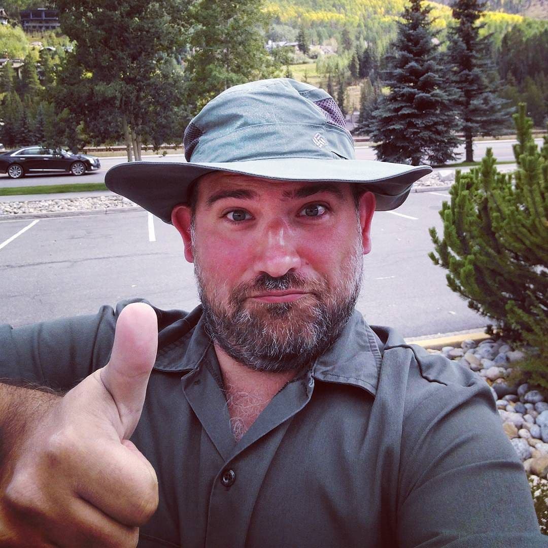 A selfie taken near Vail, Colorado. I am wearing a green soft-brim hat and a green shirt, and am making a weird face while giving a thumbs up.