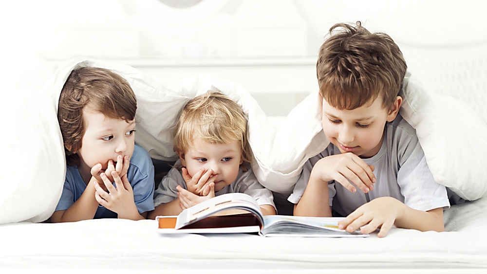 3 kids in a bed reading a book