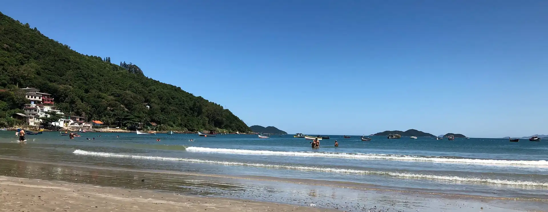 Foto da areia da praia com mar ao fundo e morro verde ao fundo