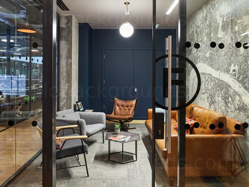 Intimate meeting room enclosed by floor to ceiling interior windows with assorted seating and daylight lighting Skype background