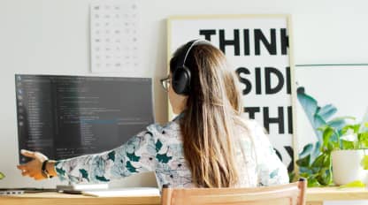 Two people sitting at 2 computers with code on the screen and a cup of hot coffee
