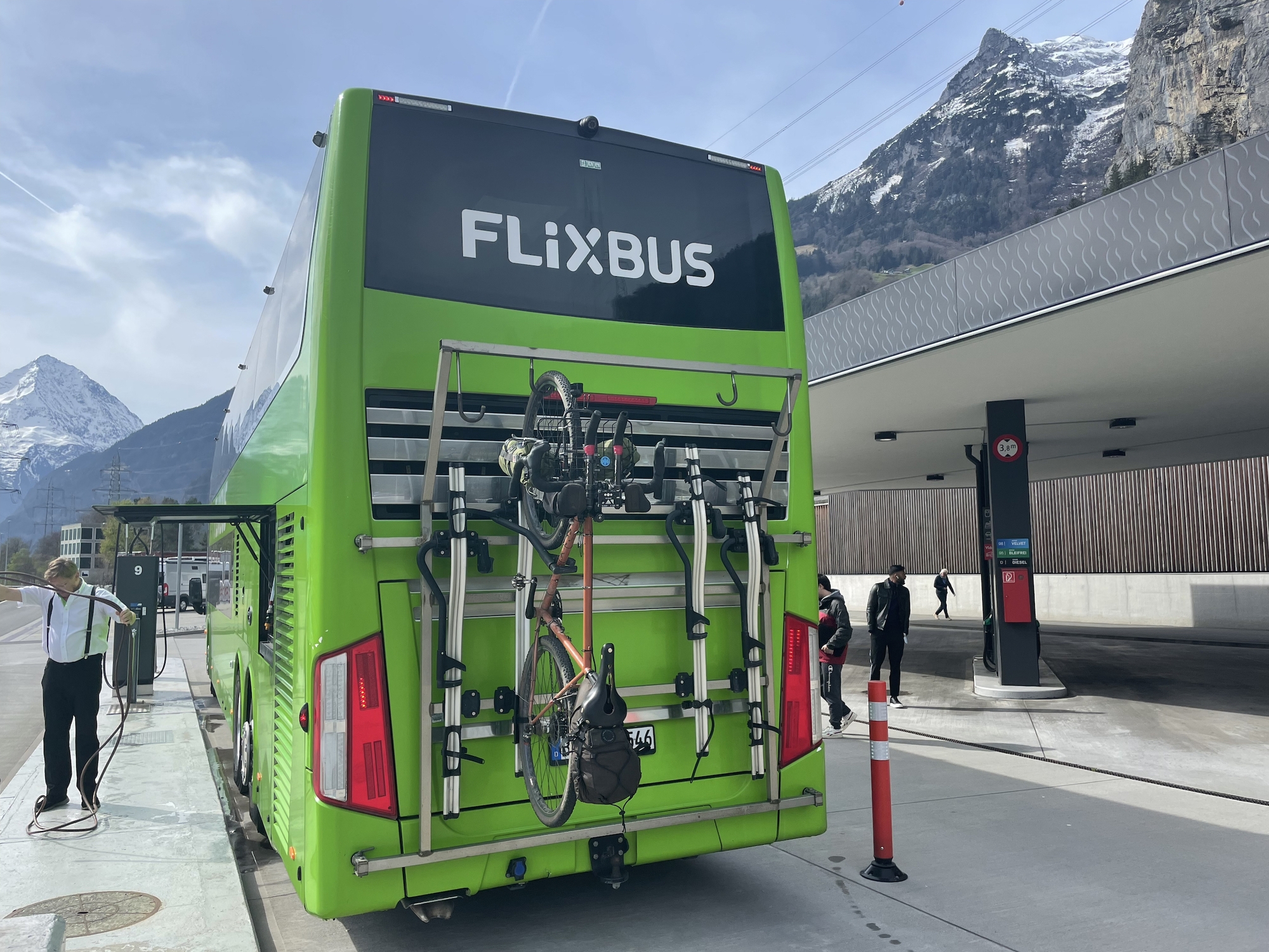 Big green Flixbus coach amongst the Alps. My bicycle on the back securely attached to a rack.