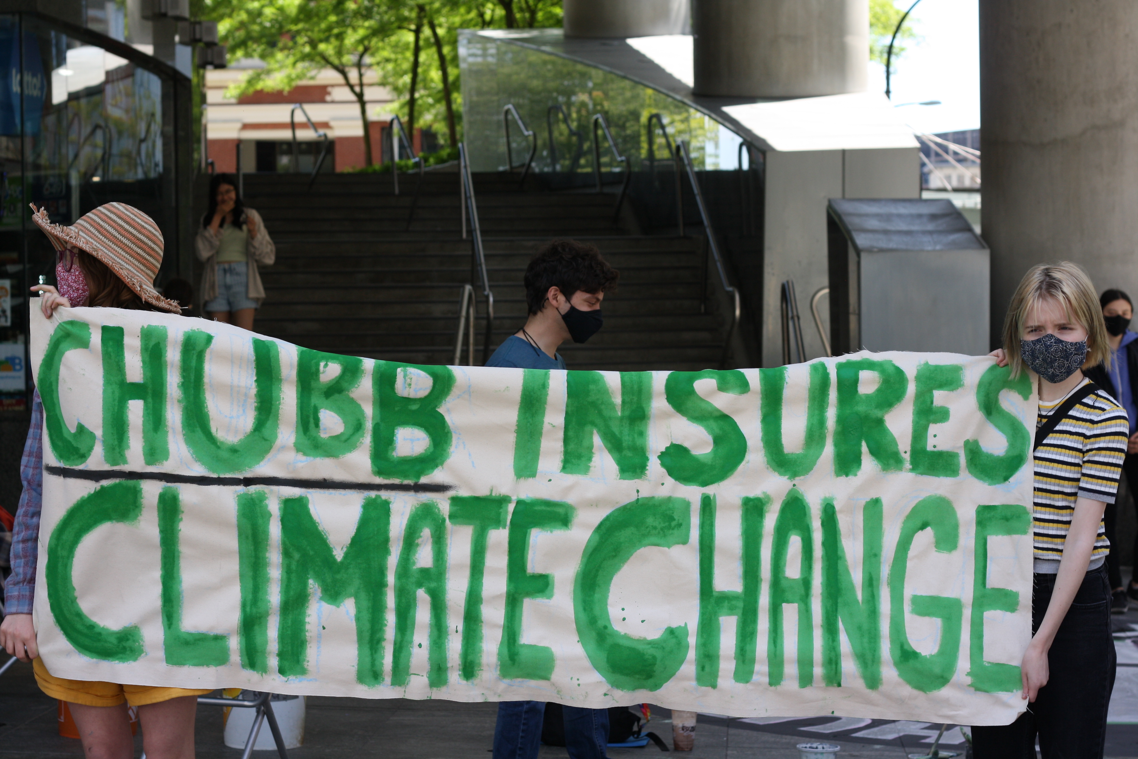 Sustainabiliteens members holding up a poster outside of the Downtown Vancouver Chubb Insurancing office, stating Chubb Insures Climate Change.