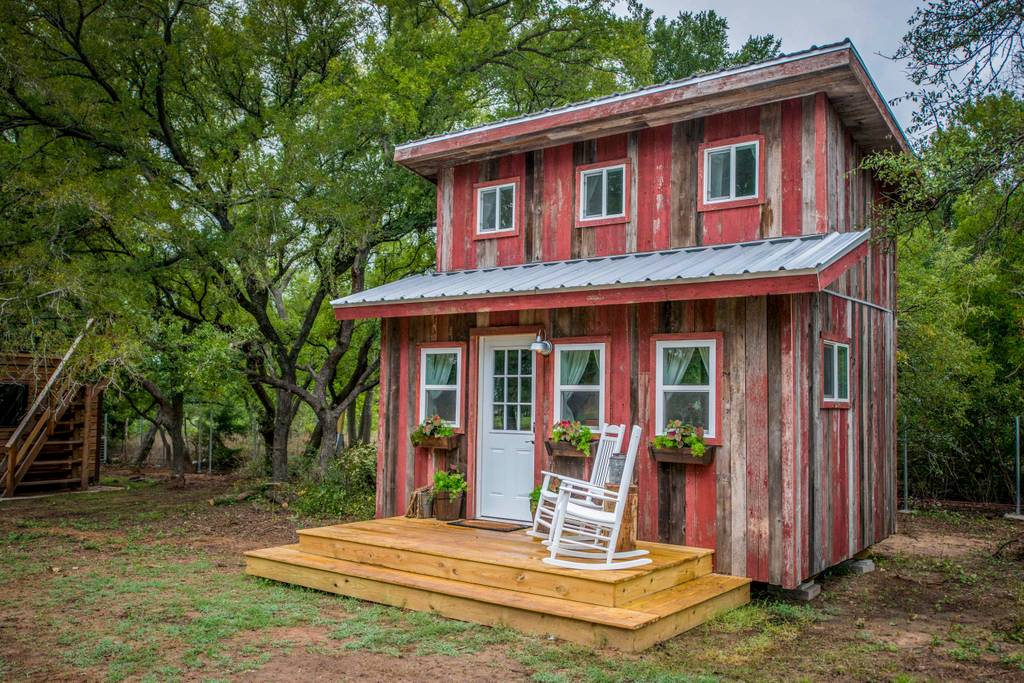 Outside of the Little Red Hen Cabin in Texas, showing a two-story tiny house and two-tier height wood front porch. Outside of the Little Red Hen Cabin in Texas, showing a two-story tiny house and two-tier height wood front porch.