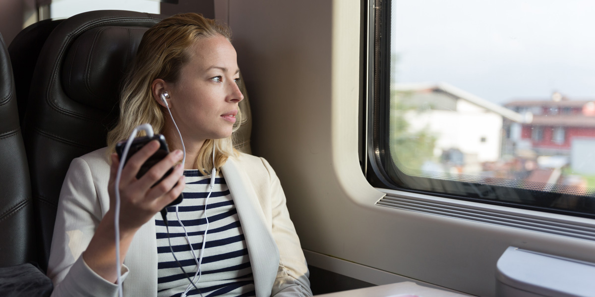 Top data science podcasts for data enthusiasts A woman sitting on a train, looking out the window with earphones in, listening to something on her phone