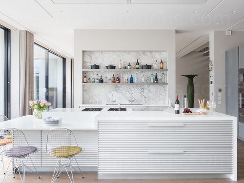 Modern kitchen decorated in white featuring kitchen island with bottled beverages on rear shelves Google Meet background