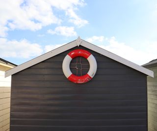 A grey beach hut with a white roof that has a red and white life ring attached to it.