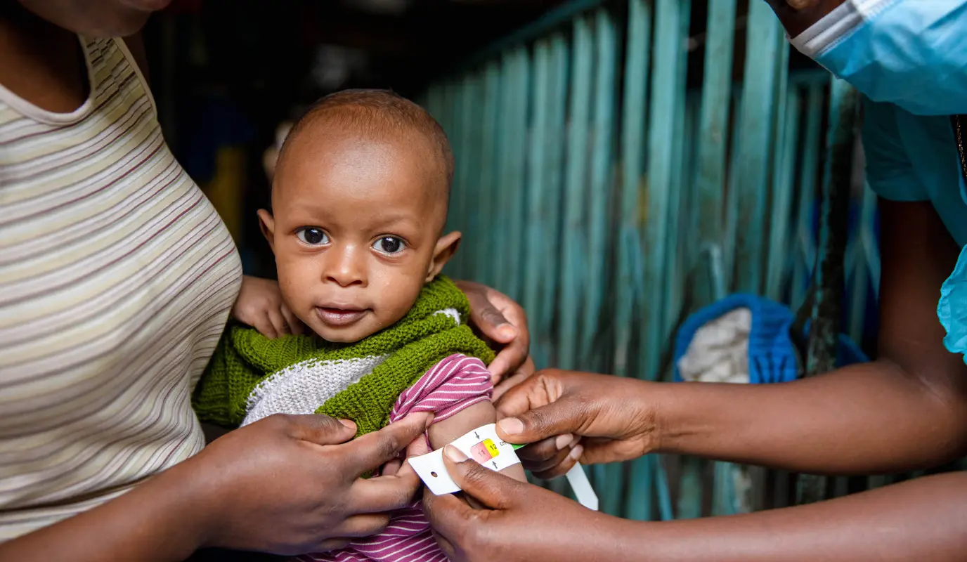 Jane Wanjiru holds her baby Mark (11 months) as a nurse uses a MUAC band to check his nutrition status