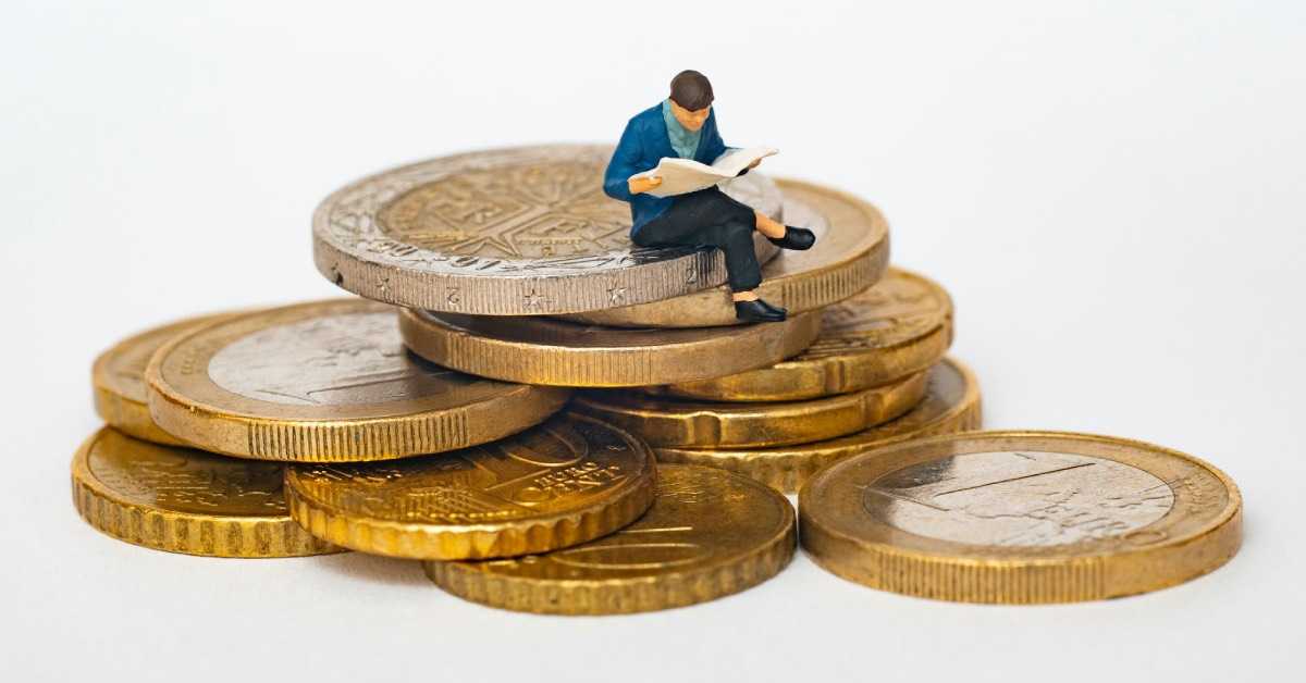 Eine kleine Modellfigur sitzt lesend auf einem Stapel Euromünzen, um die Vereinskasse zu prüfen