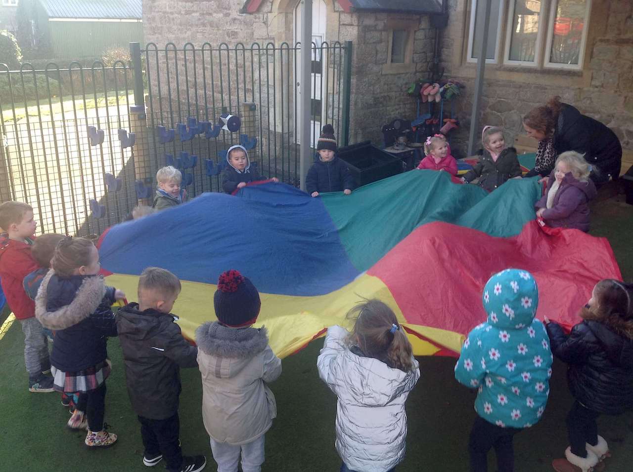 A group of children playing outside, with a colourful parachute