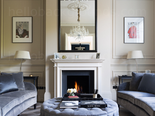 Classy living room decorated with cream walls featuring a white fireplace with two blue velvet sofas and footrest Google Meet background