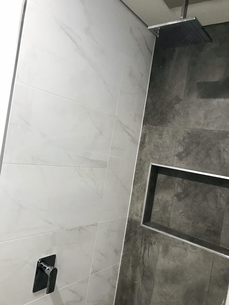 A shower with grey tiles, a new shower head, and a shelf inset into the wall.