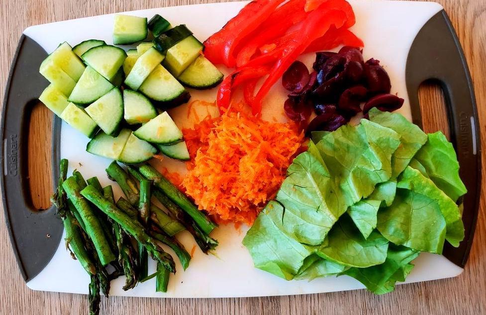 Cutting board with cucumber, lettuce, olives, carrot, asparagus, and red pepper.