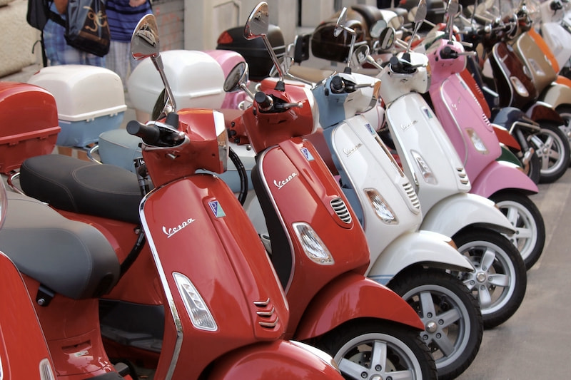 Several e-scooters parked next to each other on a street in red, pink and white colors.