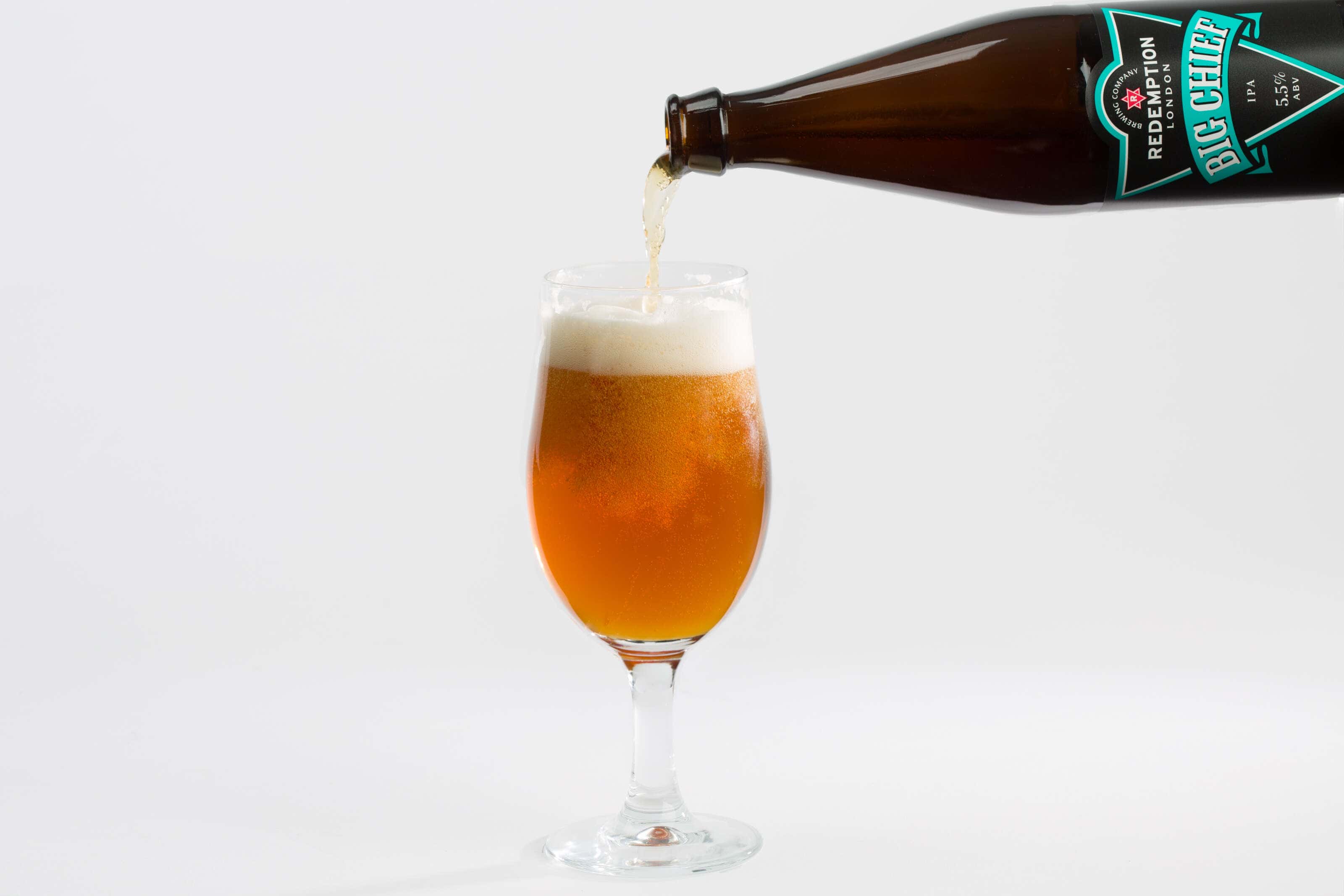 Redemption Brewery bottle of Big Chief being poured into a glass photographed in a studio with a white background.