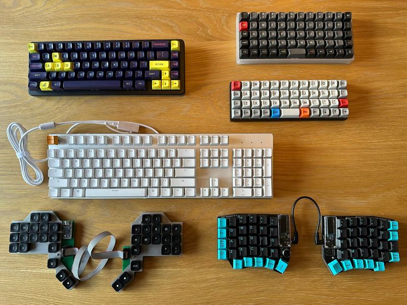 A display of my mechanical keyboard collection. There are five displayed. Two ortholinear, one compact ANSI layout. One full size ANSI layout, and two splits.