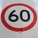 Shiny reflective speed limit sign. Black digits, red ring, with a limit of sixty.