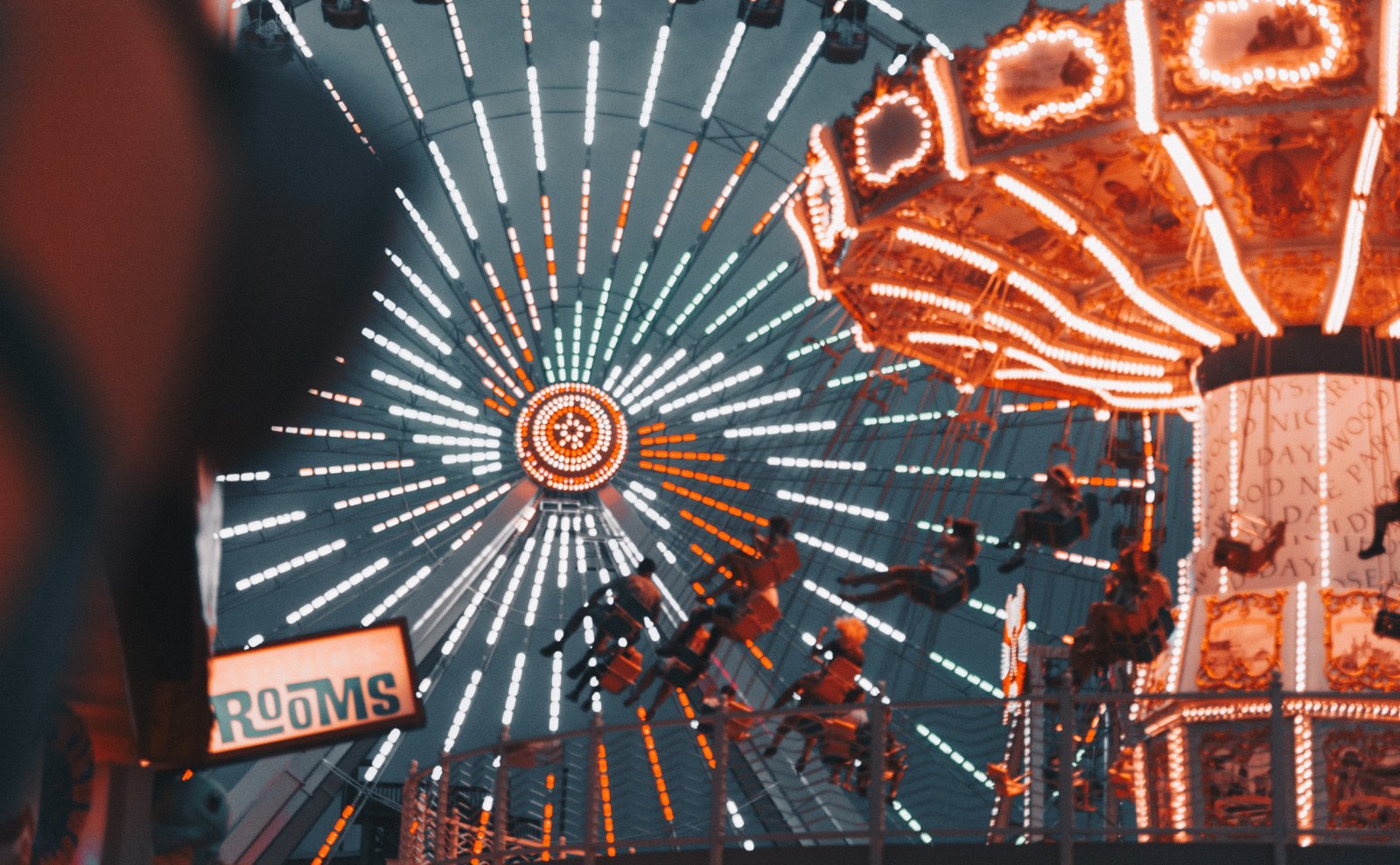 a swing ride and a ferris wheel lit up with white, blue, and orange lights at night