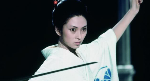 A close-up screenshot from the film 'Lady Snowblood' of a woman in a white kimono holding a katana, Yuki (played by Meiko Kaji).