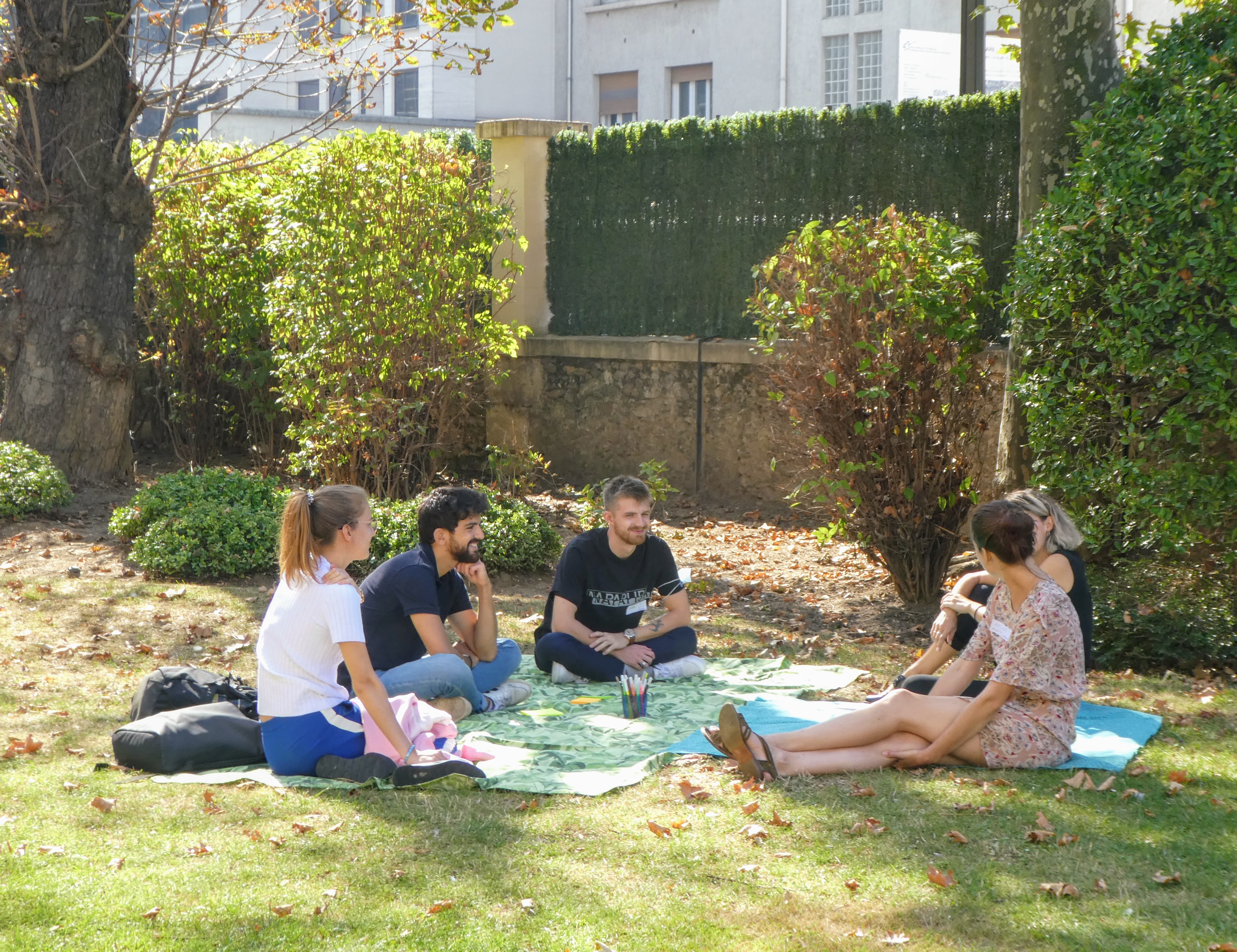 Cinq personnes discutent, assises dans l'herbe. Elles sont souriantes.