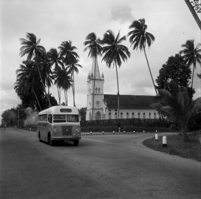 A black and white photo of a single decker bus belonging to the Ponggol Bus Service driving past the Church of The Nativity of the Blessed Virgin Mary at Upper Serangoon Road.