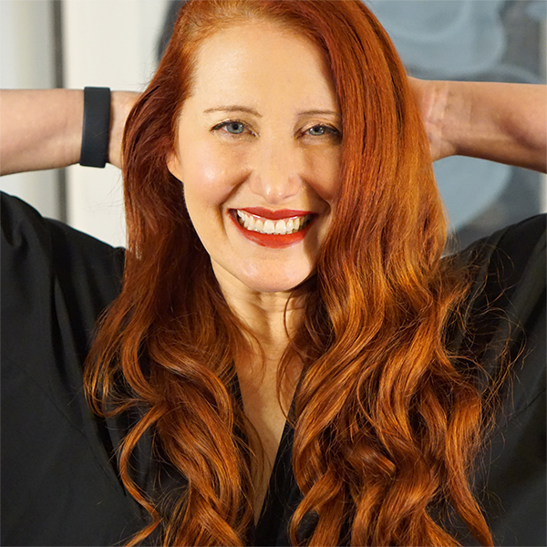 Vanessa Kelly • A smiling, readheaded woman facing the camera with hands behind her head.