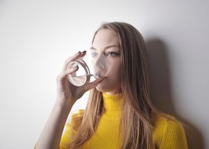 A woman drinking a glass of water to help alleviate the symptoms of dry mouth