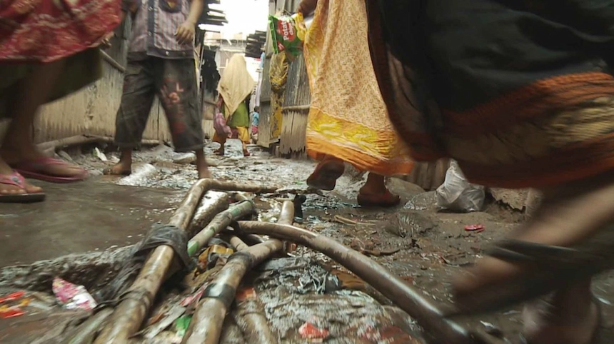Women step over water pipes in a Dhaka slum.
