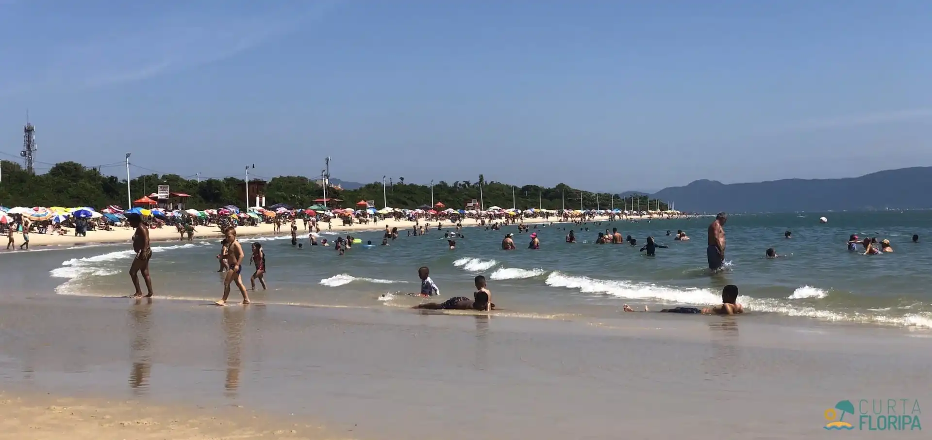 Praia da Daniela pegando toda curva da praia, banhistas e mar a direita