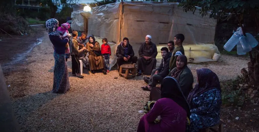 Syrian refugees gather outside of an informal tented settlement in Lebanon as night falls.