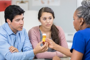 Serious senior African American female healthcare provider discusses drug side effects with a teenage female patient and the girl's father contraceptive safe sex
