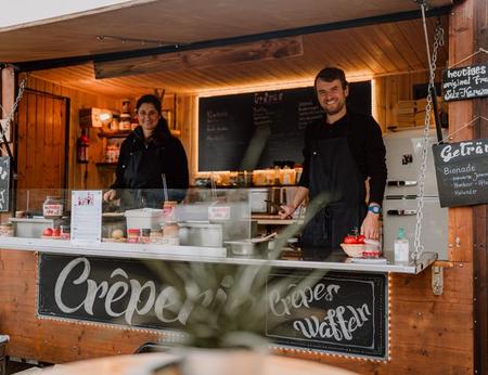 Zwei lächelnde Mitarbeiter strahlen die Gäste bei einem Catering im Food Truck an