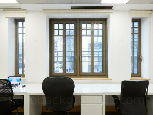 Simple shared office space containing multiple classic style windows with white multi-desk and black office chairs Google Meet background