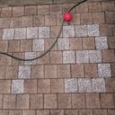 A garden hose snakes across chalk shaded outdoor pavers, as pixels the pavers spell seventy nine in big digits. A bright red plastic ball rests against the hose.