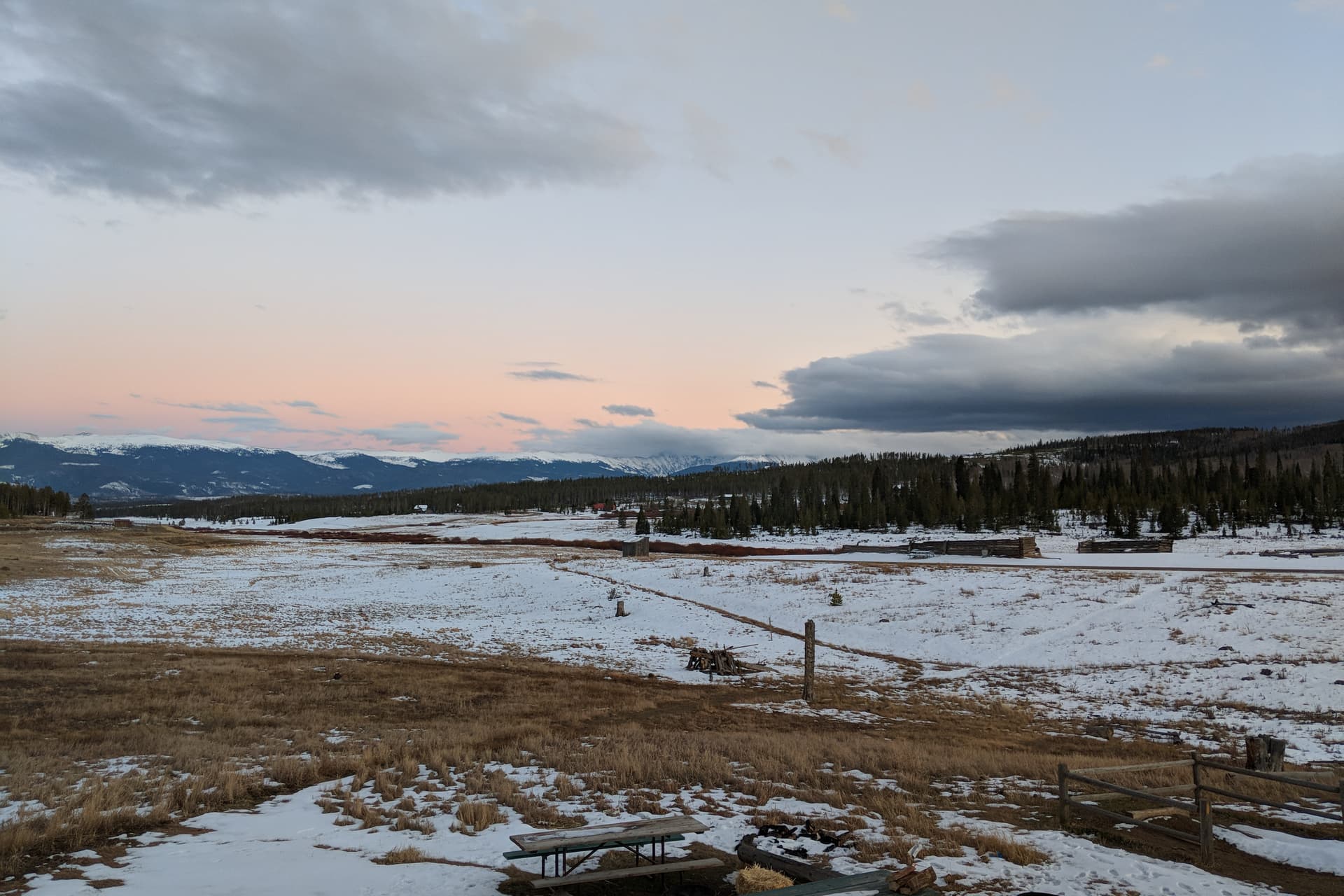 Looking out across a snowy high country ranch at sunset. In the distance, the Rocky Mountains.