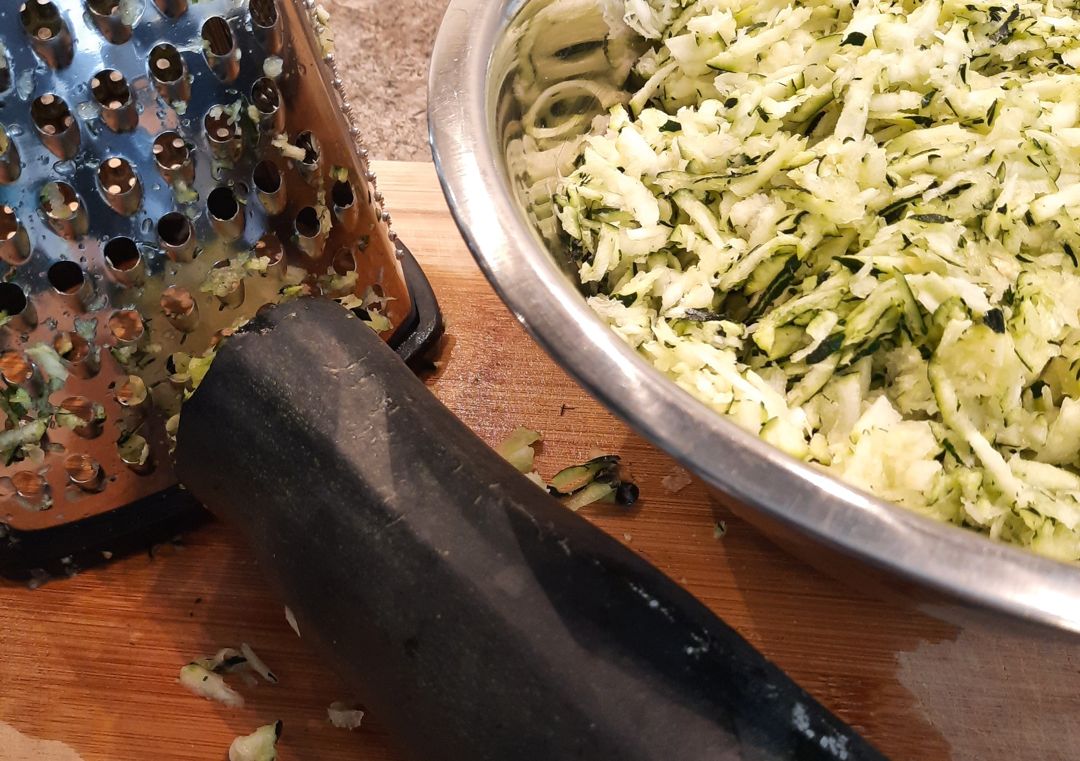 Zucchini being grated into a bowl