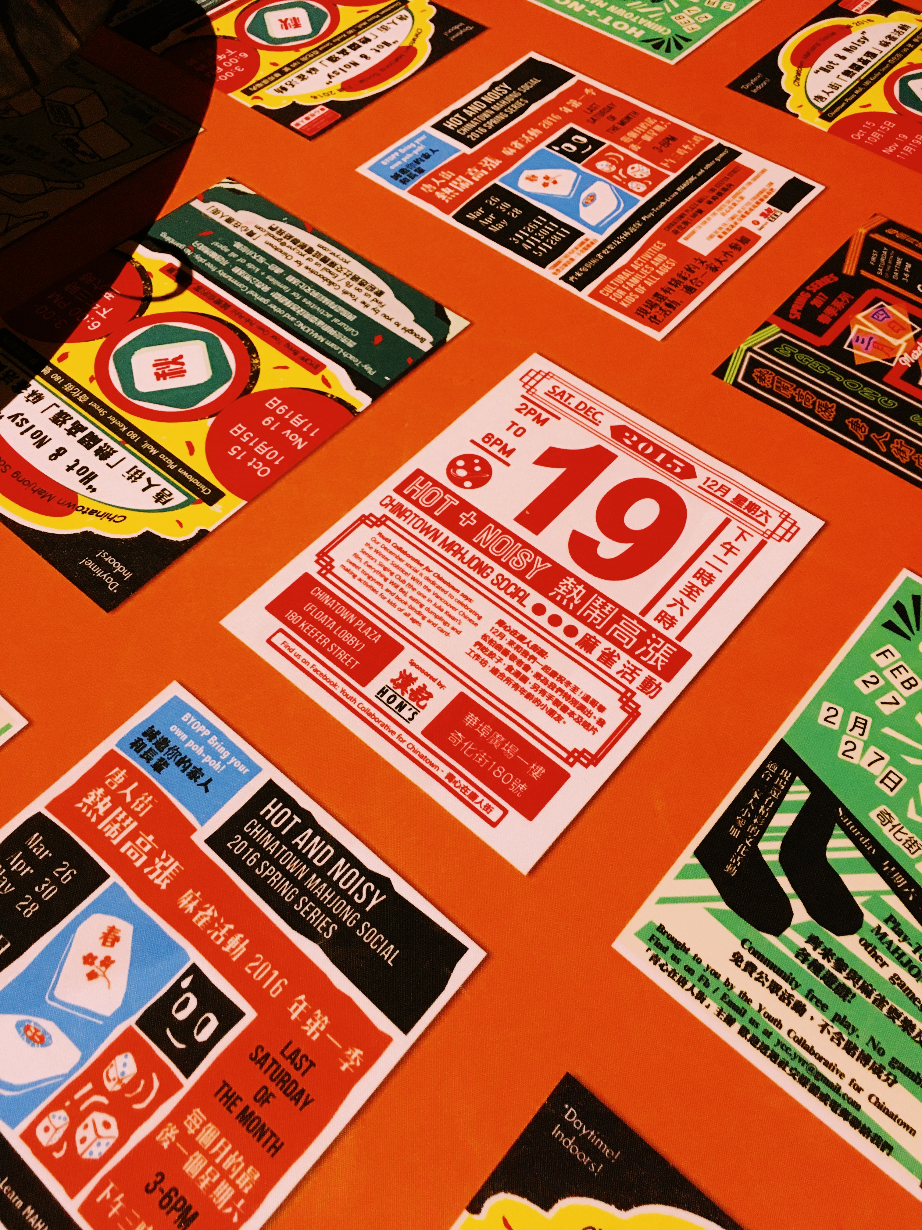 A bunch of event posters in English and Chinese, featuring bold graphic design, on top of a bright orange tablecloth.