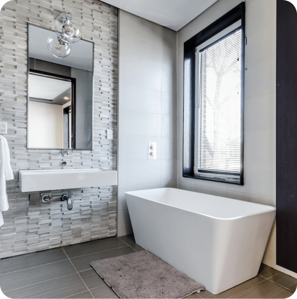 Imagen de un baño moderno. Se ve una bañera minimalista junto a una ventana. Las paredes combinan ladrillo gris y azulejos blancos.