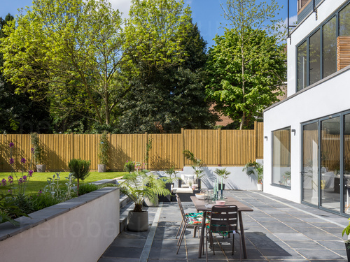 Spacious garden grey stone tiled patio with outdoor seating next to modern architectural home  Skype background