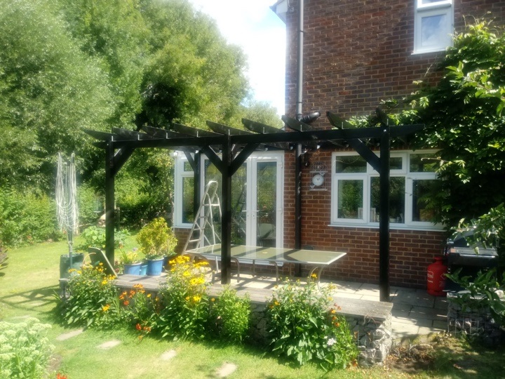 A stand alone pergola with dark stain adjacent to customer's house and conservatory