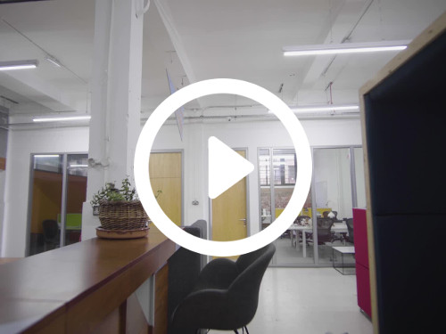 Communal workspace featuring wooden bar bearing potted plant with black stools in front of semi-open offices Skype background
