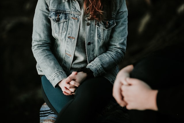 Person wearing a blue denim jacket in therapy with hands folded over her body gently