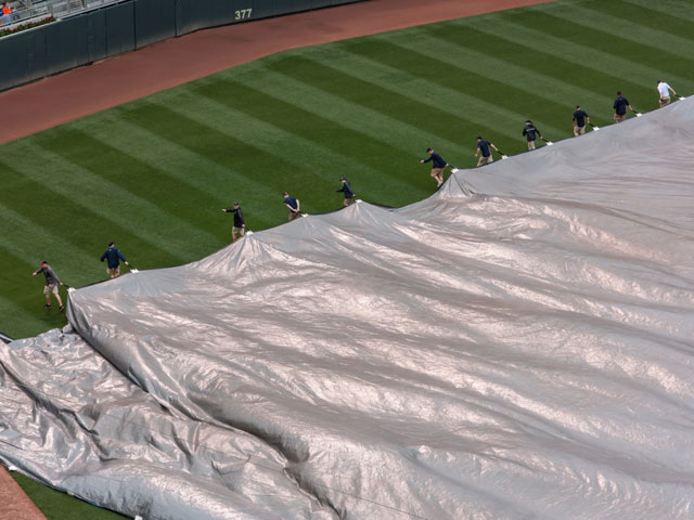 A grounds crew pulling a tarp over the baseball diamond and into the outfield during a rain delay as the game gets postponed.