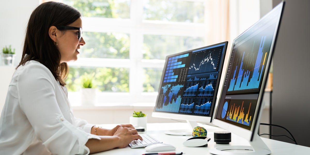 What is the XLOOKUP function in Excel? How does it work? A data analyst in side profile, sitting at a desk with two large desktop screens