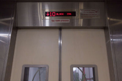 Above a lift door, a digital screen indicates the lift coming down from the tenth floor.