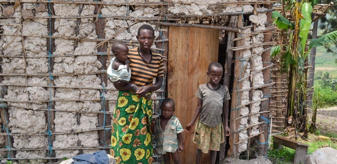 Alphonsine Mukeshimana with her family beside the structure they live in, Rwanda.